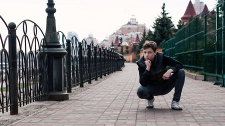 Stylish young man sitting near a fence on the waterfrontの写真素材