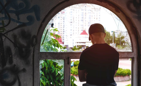 young man looks into an old broken window on the streetの写真素材