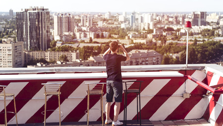 A young man observes through binoculars on the roof of a tall buildingの写真素材