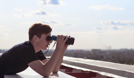 A young man with binoculars watching from the roof of a tall houseの写真素材