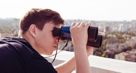 A young man with binoculars watching from the roof of a tall house