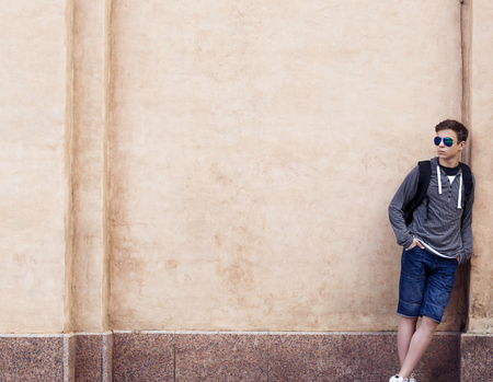 Stylish teenager with a backpack standing against the wallの写真素材