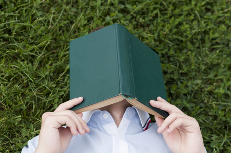 Teenager with a book in hands lying on a green grassの写真素材