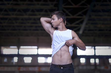 Handsome muscular guy in a white T-shirt  with jeans, standing in the gymの写真素材