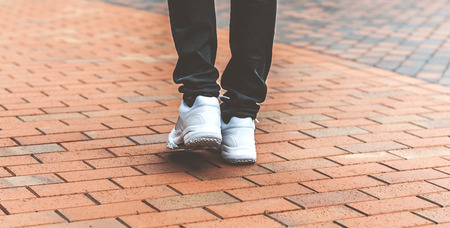 lower part of the male legs in white sneakers on the road made of bricksの写真素材