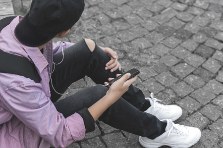 young man in a pink shirt, with a phone sitting on the sidewalkの写真素材