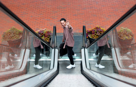 cheerful young man with a backpack on an escalator, went downstairsの写真素材