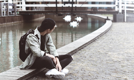 stylish teenager sitting on the sidewalk near the lakeの写真素材