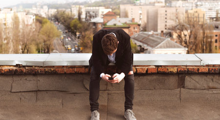 young man with a phone on the roof of a tall building