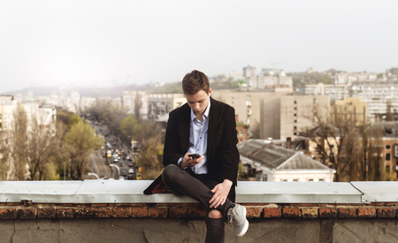 young man with a phone on the roof of a tall buildingの写真素材