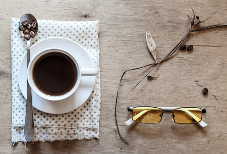 white cup of coffee on a wooden table, yellow glassesの写真素材
