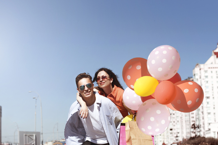 happy man and woman with shopping and balloons on a sunny dayの写真素材