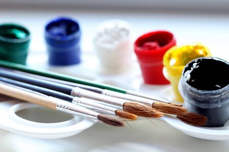 Tools for creativity on a white wooden background. Watercolor paint. Colored paints with brushes on a white palette. Back to school Children's painting concept. Children's art. Side view.の写真素材
