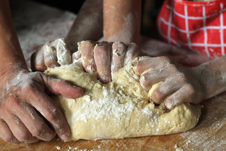 Hands of mother and daughter kneading dough together in the kitchen. Mother teaching daughter how to...
