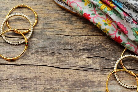 Indian jewelry bracelets and floral ethnic fabric lie on a wooden background. Bracelets with white pearls and gold. Top view. Copy space.の写真素材