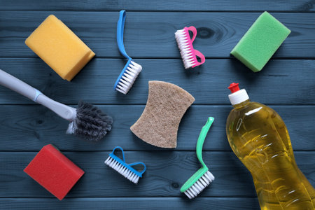 Housewife tools for cleaning. Sponges for cleaning, detergent, scrubbing brushes on dark blue wooden table background. flat lay. Concept of planning and organizing kitchen spaceの写真素材