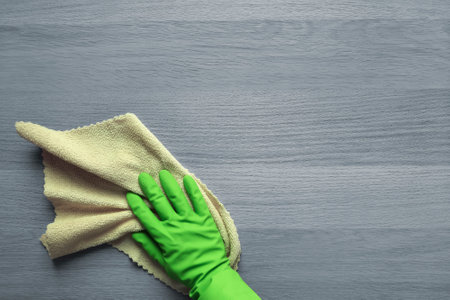 kitchen duty. copyspace. top view. Concept of daily cleaning, washing. Green rubber-gloved hand tackles gray wooden table with microfiber cloth. flat lay.の写真素材