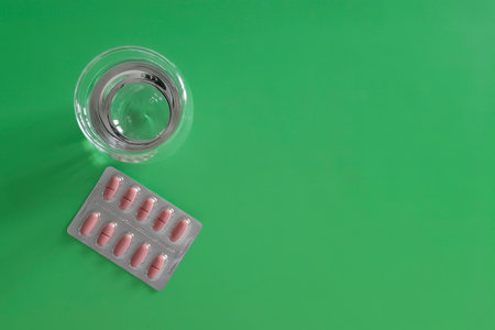 Tablets and glass of water. Pills in package and water on green background. vitamins and medicines. Concept of health, treatment, disease prevention. copyspace. top view.の写真素材