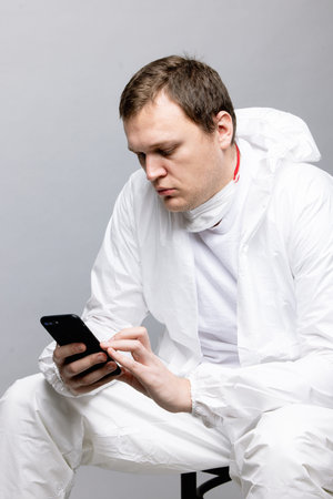 Tired doctor wearing mask and gloves at the hospital in coronavirus times, checking his smartphone.