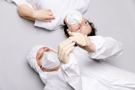 Two tired doctor male and female in a protective suit on the floor, exhausted in the fight against a pandemic covid-19の写真素材