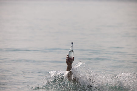 Bottle with pure water in the hand in ocean and splash around itの写真素材