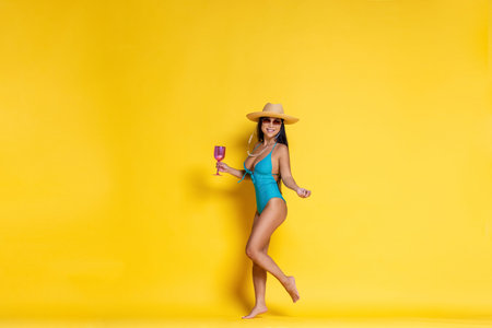 Beautiful asian girl in swimsuit and a hat with wineglass in her hand on a yellow background