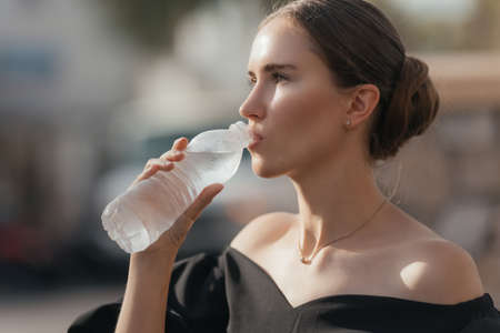 Close-up portrait of a beautiful young girl drinking water from the bottle. Street portrait.の写真素材