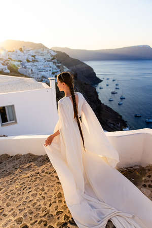 Young girl with long hair in white dress on Santorini island. Dawn. Sunrise.の写真素材