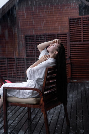 Young girl in white dressing gown under the rain in the Maldives. Bungallow at the background. Island. Rain in the Maldives.の写真素材