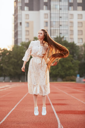 Attractive girl with red long hair, slender and beautiful posing for a photo in a city landscape. Sunrise portrait. Dawn.の写真素材