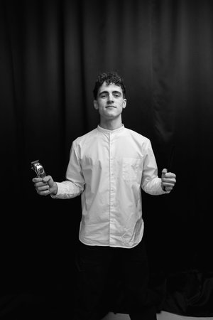Barber holds in his hands a clipper and a comb