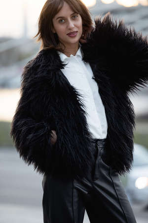 Outdoor fashion portrait of young beautiful girl wearing trendy black faux fur coat. Protect animals. Stop wearing fur.の写真素材