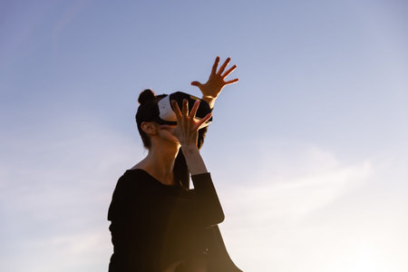 Young woman uses virtual or augmented reality glasses in magic atmosphere of dawn rays, female VR...