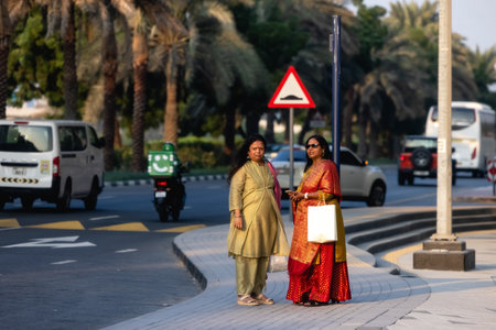 Dubai, UAE - January 20221: Two Indian women wearing colorful saris waiting for taxi in street in Dubaiのeditorial素材