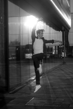 young attractive dancer in casual cloth doing ballet jump on the urban background. Contemporary dance, modern choreography.の写真素材