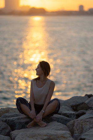 Woman practicing yoga meditation at sunrise. Morning yoga on the beach or coast of sea urban city background.の写真素材