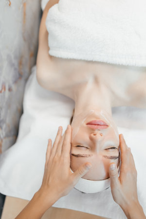 Shot of cosmetologist making face massage for rejuvenation to woman while lying on a stretcher in the spa center. Relaxed young female is resting on couch while cosmetologist massaging her faceの写真素材