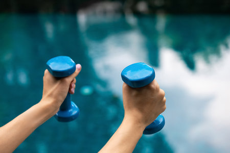 Womans hand holding blue dumbbell isolated on turquoise pool background. Equipment for home workout. Fitness outdoors and activity. Sport and healthy lifestyle concept. Copy space in right sideの写真素材