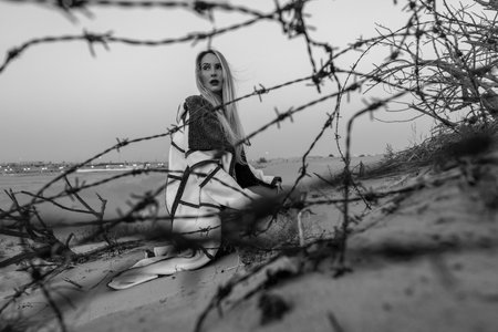 Girl sitting behind the barbed wire and look forward. Desert landscape. The concept of hopelessness. Depression. social issues and psychological problems. gender rights mental health, equalityの写真素材