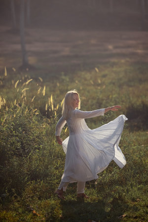 A beautiful fifty-year-old woman with light hair, dressed in white clothing and stone bead necklaces, is looking into the frame.の写真素材