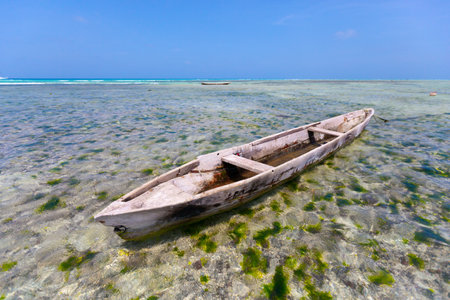The scene depicts an aged wooden boat gently floating on the crystal-clear waterの写真素材