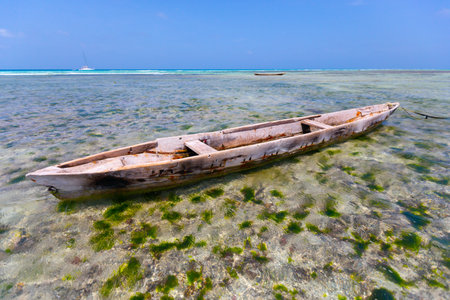 The scene depicts an aged wooden boat gently floating on the crystal-clear waterの写真素材