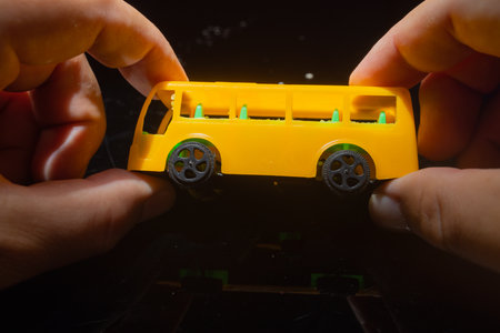 A man holds a plastic model of a yellow school busの写真素材