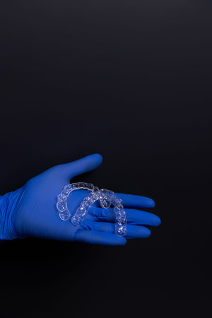 A dentist in blue rubber gloves holds transparent plastic aligners