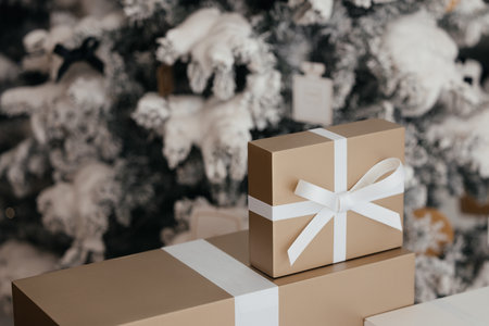 A gift box under a snow-covered Christmas tree tied with a white ribbon. The theme revolves around Christmas gifts, New Year, and presents from Santa.の写真素材