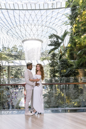 Bride in a wedding dress and a groom in a white suit standing near fountains during a pre-wedding photo session at Jewel Changi Airport in Singapore city Green conceptの写真素材
