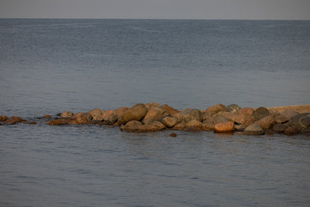 Calm blue sea and big rocks on the beach. The stones separate the photo and are in the center. The color is muted due to the fact that sunlight practically does not fall on them anymore, it is eveningの写真素材