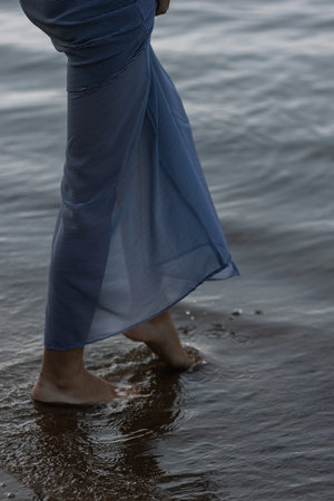 female legs a woman in a gold dress walks along the river bank waves at sunsetの写真素材