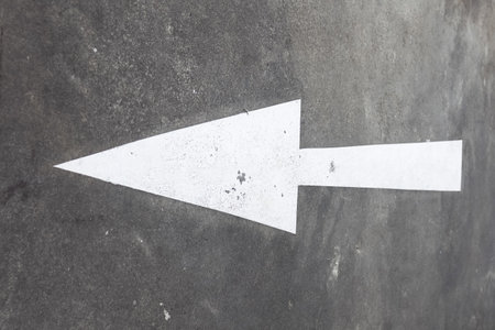 A large arrow pointing left, painted in white on an asphalt road. Road markings in the city.の写真素材