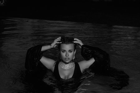 A girl in a black swimsuit poses at night by the pool at a party.の写真素材